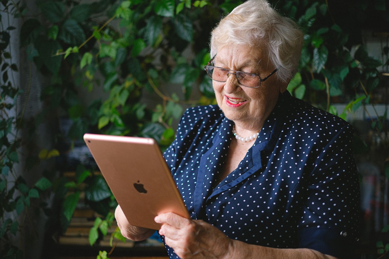 An older woman looking at a tablet she is holding, smiling